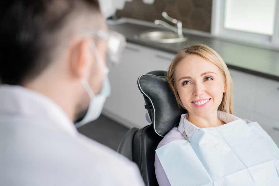 Happy young blonde female patient looking at her dentist with healthy smile