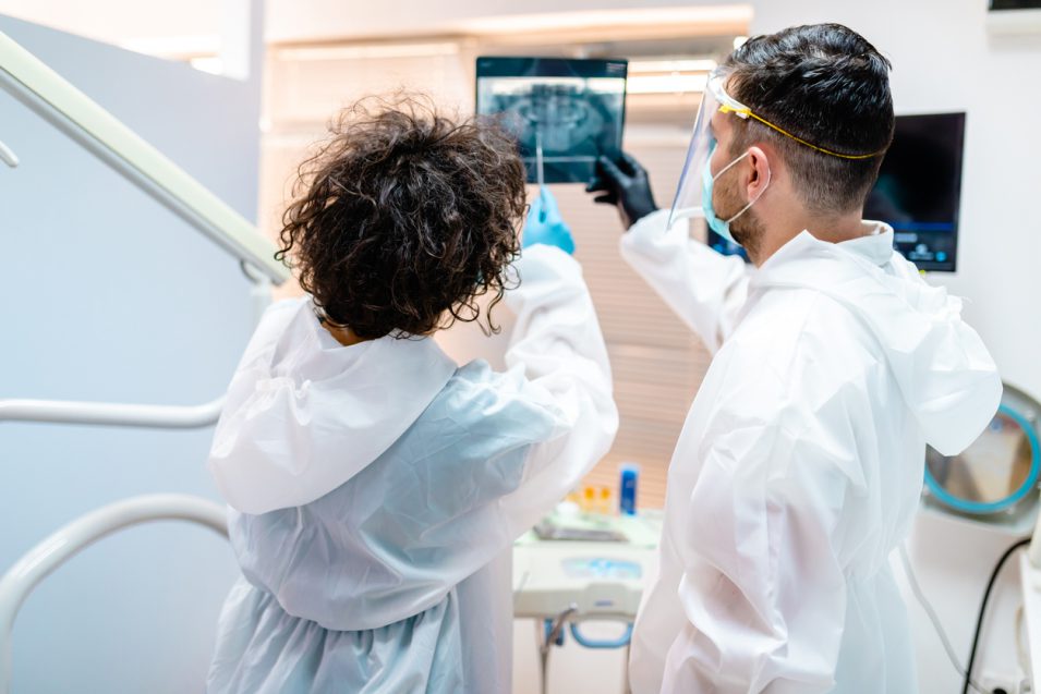 Oral surgeons in protective workwear having discussion about patients X-ray image