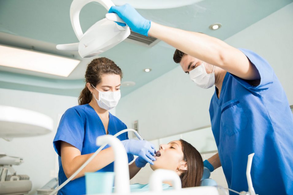 Dentist With Male Colleague Treating Patient At Clinic