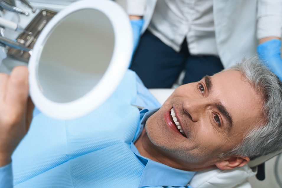 middle aged man looking dental implant in mirror