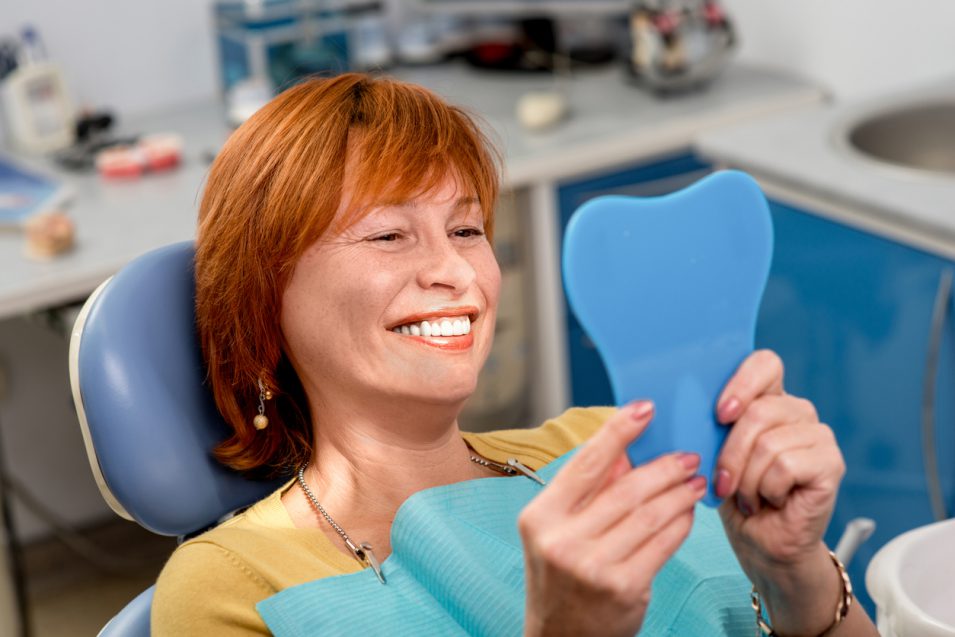 woman looking at implanted tooth in mirror in hamilton dental clinic